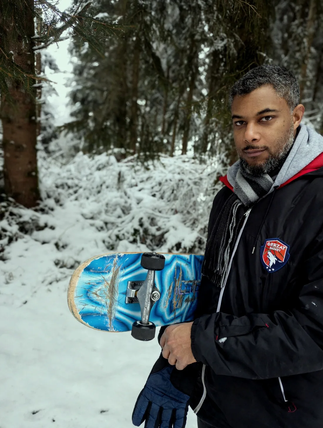 Lionel Euphrasie dans une forêt enneigée, sa planche de skate sous le bras.